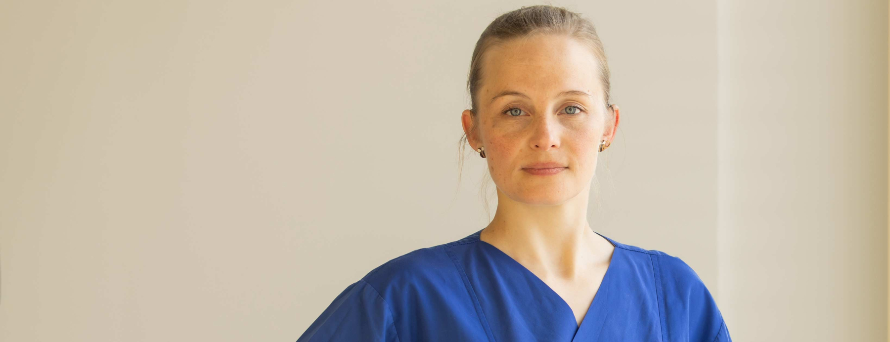 Junge Ärztin in blauem Kasack guckt direkt in die Kamera.