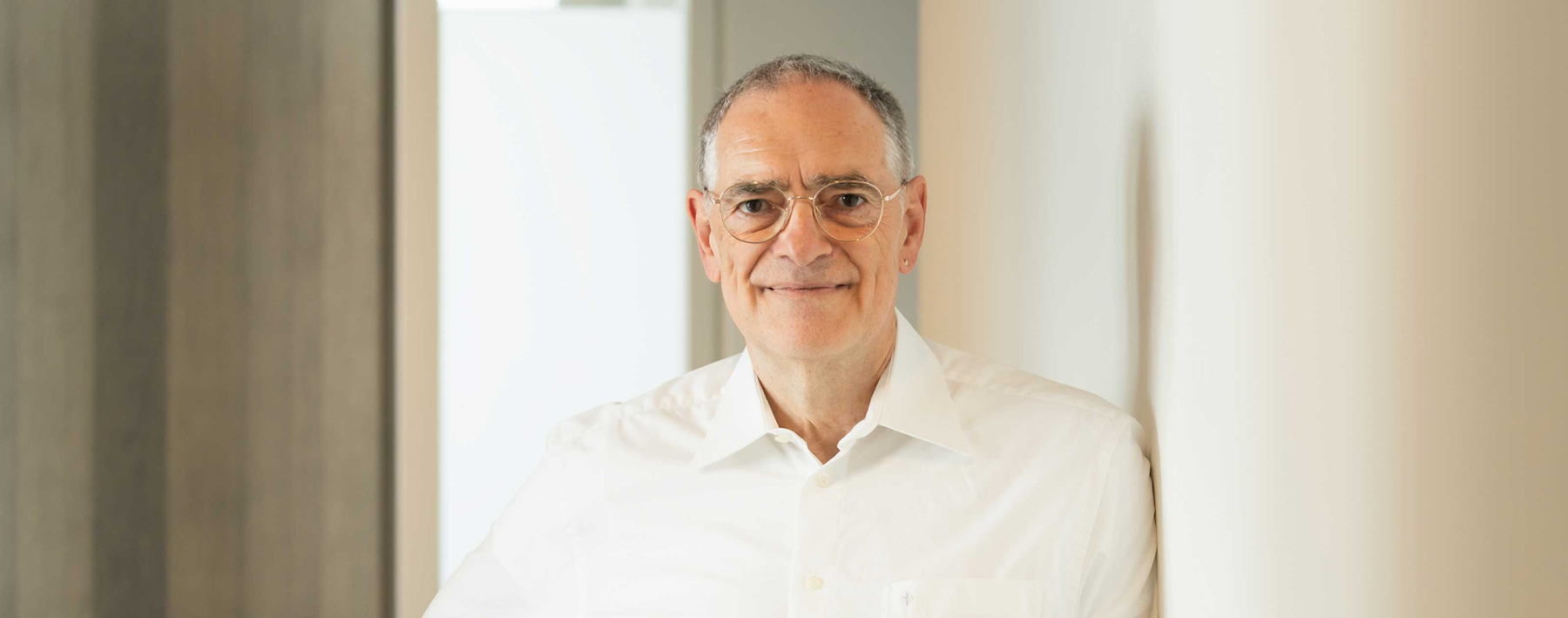 Arzt im Ruhestand mit Brille und kurzen Haaren guckt in die Kamera.