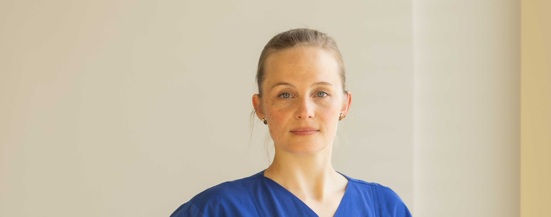 Junge Ärztin im blauen Kasack guckt in die Kamera